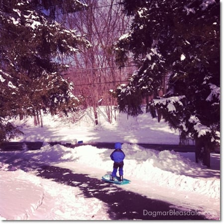 boy sledding down a driveway, standing on sled